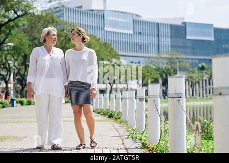 Buona madre e sua figlia adulta che camminano nel parco cittadino e discutono le ultime notizie Foto Stock