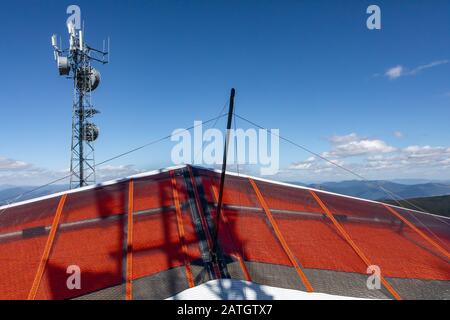 Vista ravvicinata dell'aereo delta parcheggiato a terra in cima alla collina. Lezioni di sport aereo estremo. Appendere gli alianti pronti a volare sotto il cielo blu chiaro Foto Stock