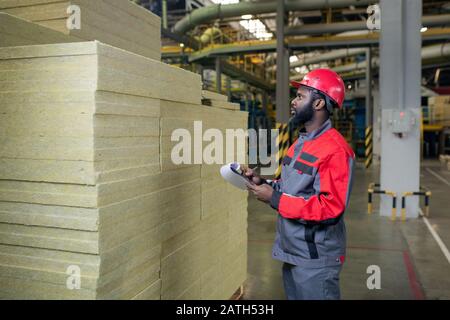 Serio giovane costruttore bearded che contava i materiali di calore prodotti e che fa le note negli appunti Foto Stock