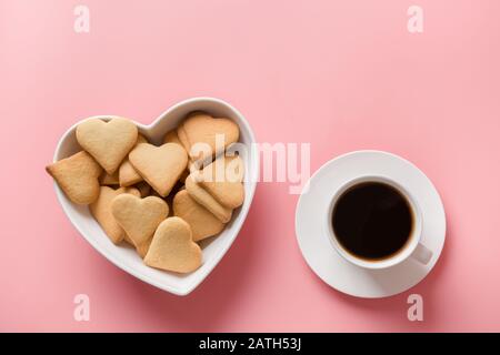 Tazza di caffè e biscotti fatti in casa in forma di piastra di cuore su rosa. Carta di San Valentino. Disposizione piatta. Vista dall'alto. Spazio per il testo. Foto Stock