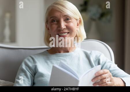 Ritratto di donna matura sorridente leggere libro a casa Foto Stock
