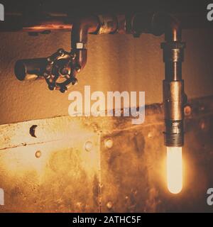Lampada di design industriale con tubi, valvole e lampadina, decorazione interna metallica con illuminazione e spot Foto Stock