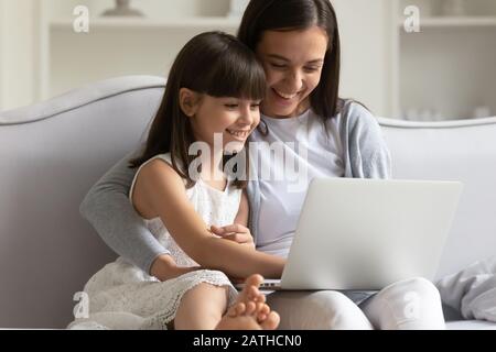 Mamma giovane felice e figlia piccola che usano il laptop a casa Foto Stock