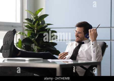L'uomo d'affari seduto sul posto di lavoro indossando le cuffie ascolta la canzone godersi una pausa Foto Stock