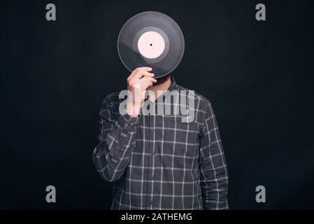 Un uomo sta coprendo il suo volto con un vinile record su sfondo nero. Foto Stock