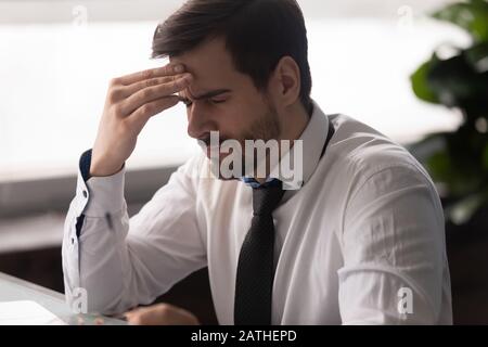 Uomo d'affari che soffre di mal di testa sul posto di lavoro sentirsi stanco e sovraccarico Foto Stock