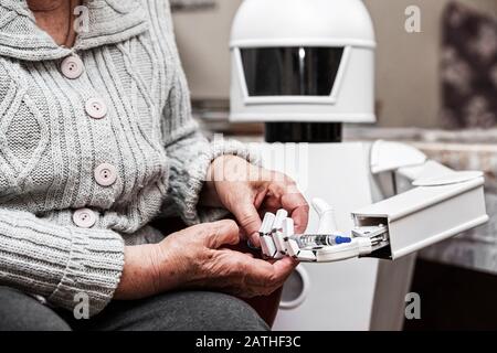 il robot autonomo caregiver sta tenendo una siringa di insulina, dandola ad una donna adulta senior nel suo soggiorno, concetto di vita assistita da ambiente Foto Stock