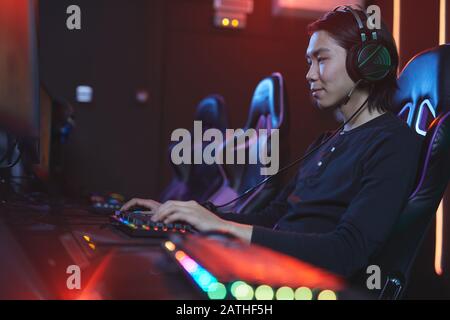 Ritratto della vista laterale di uomo asiatico sorridente che gioca ai videogiochi in studio pro-gaming, copia spazio Foto Stock
