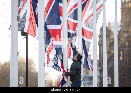 Un lavoratore rimuove le bandiere dell'Unione dai flagelli di Parliament Square, Londra, a seguito di eventi che segnano la partenza del Regno Unito dall'Unione europea il 31st gennaio. Foto Stock