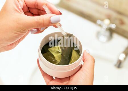 Le mani femminili stanno prendendo i cerotti dell'occhio fuori dal contenitore con le pinzette. Concetto anti invecchiamento. Foto Stock