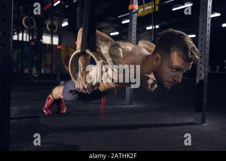 Giovane uomo sano, atleta che fa esercizi, pull-up in palestra. Singolo modello caucasico praticando duro, addestrando il suo corpo superiore. Concetto di stile di vita sano, sport, fitness, bodybuilding, benessere. Foto Stock