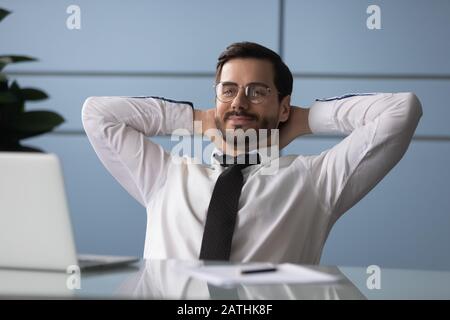 L'uomo d'affari ha messo le mani dietro la testa che riposa godere della rottura sul posto di lavoro Foto Stock