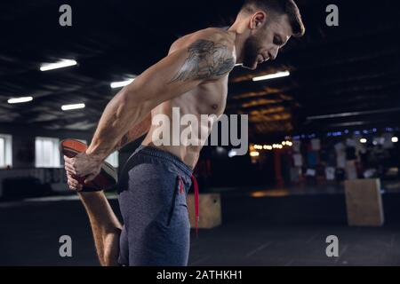 Giovane uomo sano, atleta che fa esercizi, allungandosi in palestra. Singolo modello caucasico praticando duro, addestrando il suo corpo. Concetto di stile di vita sano, sport, fitness, bodybuilding, benessere. Foto Stock