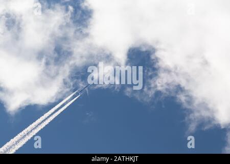 Un getto bicomotore nel cielo blu con nuvole lascia un segno di inversione. Foto Stock