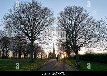 Figure femminili passeggiando nel parco retroilluminato dalla luce solare invernale, con monumento alle vittime del colera in lontananza Foto Stock