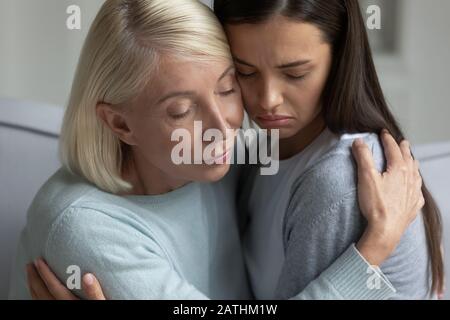 La cura della madre matura abbraccia il bambino adulto arrabbiato che mostra il supporto Foto Stock