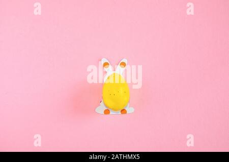 Uovo di Pasqua e sagome di carta di un coniglietto di pasqua su sfondo rosa Foto Stock