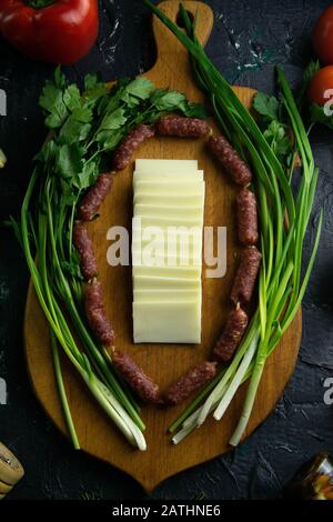 Mozzarella affettata su una tavola di legno, intorno al prosciutto, cipolle verdi, pomodoro, souce, olive, limone, spezie, aneto. Foto Stock