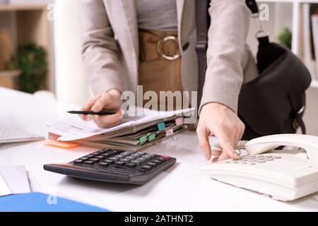 Primo piano di un manager irriconoscibile che si trova alla scrivania con carte e sta chiamando l'altoparlante Foto Stock