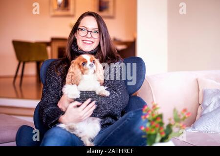 Scatto di giovane donna con il suo cucciolo carino rilassante in poltrona a casa. Foto Stock