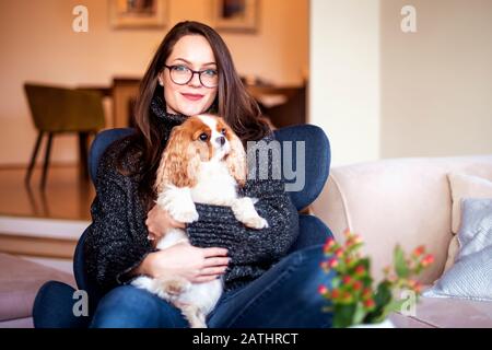 Scatto di giovane donna con il suo cucciolo carino rilassante in poltrona a casa. Foto Stock