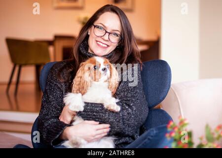 Scatto di giovane donna con il suo cucciolo carino rilassante in poltrona a casa. Foto Stock