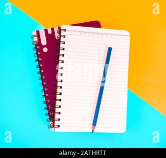Una matita di legno blu posizionata su due notebook progettati con uno sfondo di carta arancione-blu Foto Stock