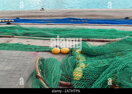 Reti da pesca blu e verdi con galleggianti gialli disposti a terra al porto con il mare sullo sfondo Foto Stock