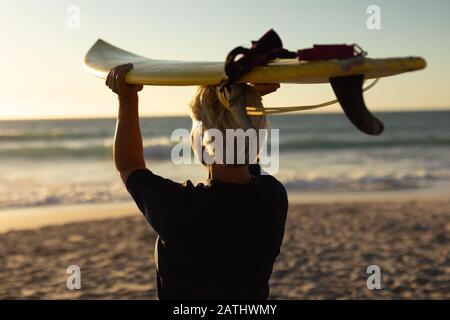 Donna anziana con tavola da surf in spiaggia Foto Stock