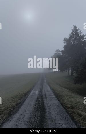 Una strada sterrata a due piste che conduce all'orizzonte su una mattina molto nebbiosa e nebbiosa. Foto Stock