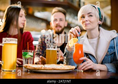 Amici sorridenti che mangiano pizza e succo di frutta, ridono e si divertono nel ristorante, colleghi millennari diversi che si godono il pranzo durante la pausa di lavoro Foto Stock