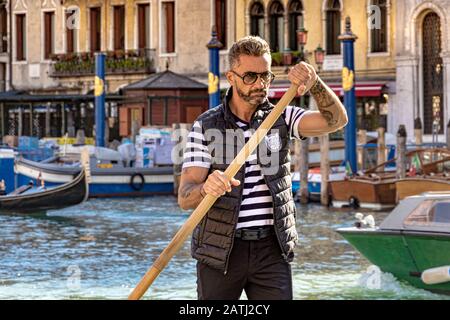 Un Gondoliere a Venezia afferra il suo remo e si concentra sullo sterzo della sua gondola lungo il Canal Grande a Venezia Foto Stock