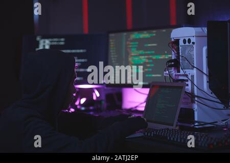 Ritratto di hacker irriconoscibile che utilizzano apparecchiature informatiche con codice di programmazione su schermi in stanza oscura, concetto di cyber sicurezza, copia spazio Foto Stock