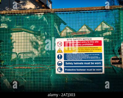 Un avviso di sicurezza di costruzione / cantiere dai colori vivaci sul cancello chiuso di uno sviluppo urbano di alloggi nel Regno Unito Foto Stock