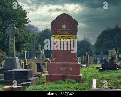 Una lapide di granito rosso pericoloso/pericoloso su una tomba nel cimitero di Flaybrick a Birkenhead, Regno Unito. Preso in inverno in un giorno coperto. Foto Stock