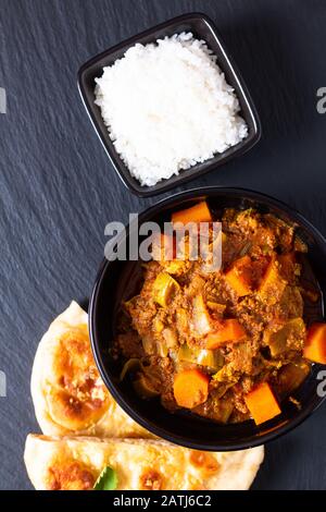 Concetto di cibo orientale speziato terra o tritato Beefs masala curry con pane naan e riso su sfondo di ardesia nera Foto Stock