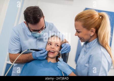 Il dentista dei bambini verifica i denti delle ragazze, mentre sedette sulla sedia dentale all'ufficio. Concetto di assistenza sanitaria. Foto Stock