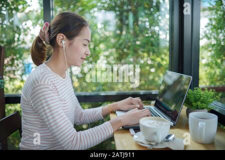 Giovane donna freelance utilizzare un laptop e cuffie editing video filmati nel bar questo è lo stile di vita del creatore di contenuti Foto Stock