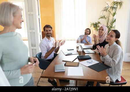 Gli impiegati multirazziali felici applaudono il ringraziamento del presentatore femminile per la riunione Foto Stock