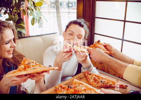 La compagnia di ragazzi nella pizzeria. Ragazzi allegri con pizza nelle loro mani. Studenti in un bar Foto Stock