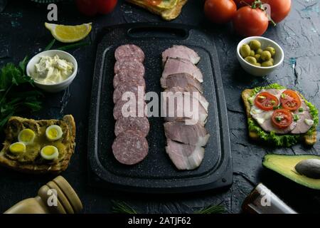 Tagliere grigio con salame e prosciutto. Intorno pomodoro, souce, olive, limone, olio d'oliva con spezie e panini Foto Stock