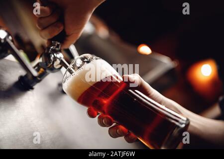 Barman versa birra artigianale da bere da rubinetto in vetro, sfondo scuro Foto Stock