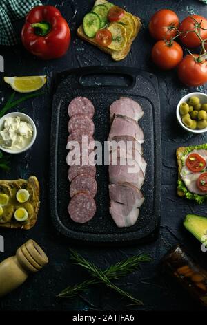 Tagliere grigio con salame e prosciutto. Intorno pomodoro, souce, olive, limone, olio d'oliva con spezie e panini Foto Stock