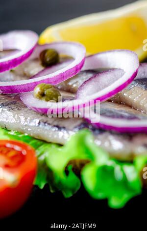 Appetitosi smorrebrod con aringa norvegese, lattuga, cipolla blu, limone e pomodoro si trovano su una tavola di legno Foto Stock