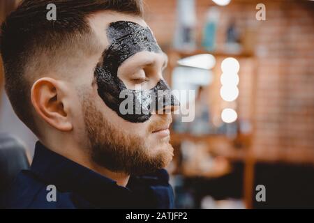 Bell'uomo con maschera facciale di carbone nero, cura di concetto della pelle, pulizia dei pori da acne Foto Stock