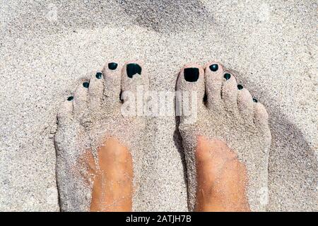 Primo piano dei piedi di una donna coperti di sabbia sulla spiaggia Foto Stock
