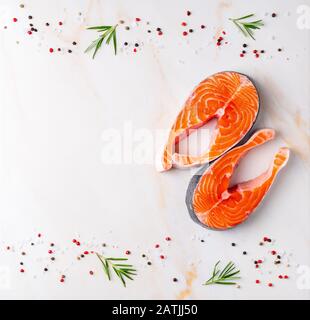 Fondo alimentare, bistecche di salmone e condimenti su tavolo di marmo bianco crema, piatto, spazio copia Foto Stock
