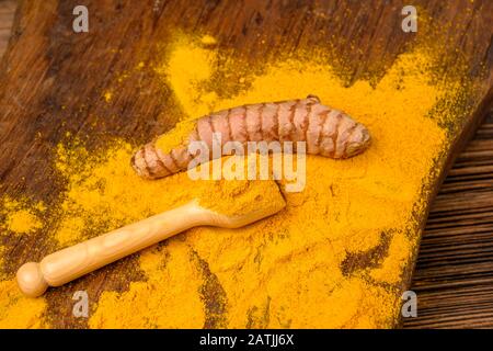 Polvere di curcuma essiccata con un cucchiaio di legno e una radice curcuma fresca davanti ad uno sfondo di legno. Foto Stock