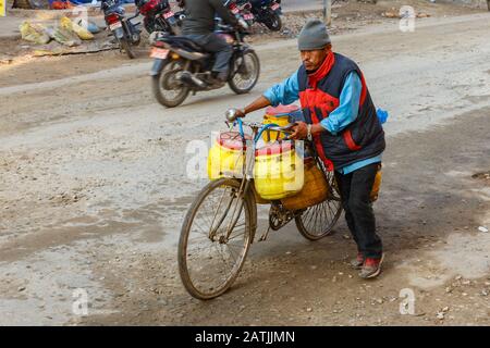 Katamandu, Nepal - 13 novembre 2016: Un uomo nepalese spinge la sua bicicletta completamente carica di barili gialli lungo la strada a Kathmandu. Foto Stock