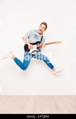 Giovane rocker che suona su chitarra elettrica, mostrando lingua e salto Foto Stock